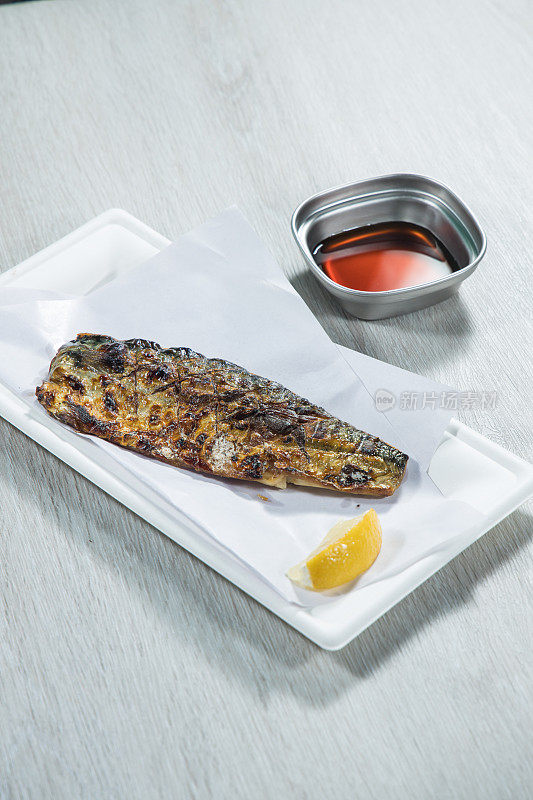 Fried mackerel with lemon and soy sauce on white plate